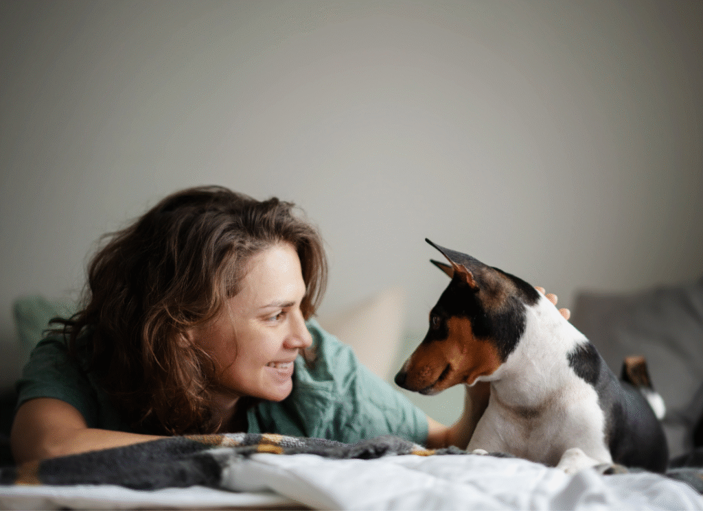 Trygghet och harmoni i hemmet En kvinna ligger på sängen och ler mot sin hund i en lugn hemmiljö.