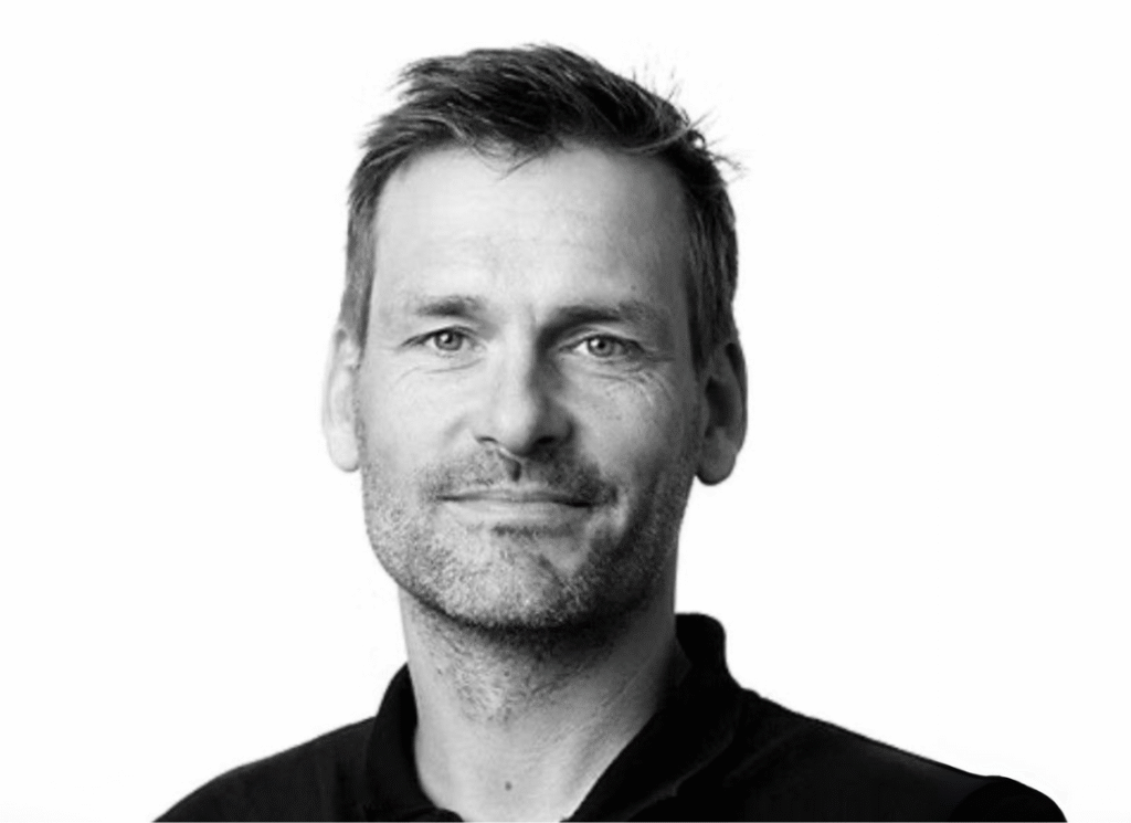 Porträtt av en man i svart tröja mot ljus bakgrund, fotograferad i svartvitt.